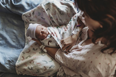 Overhead view of mother holding newborn boy with hat in hospital bed