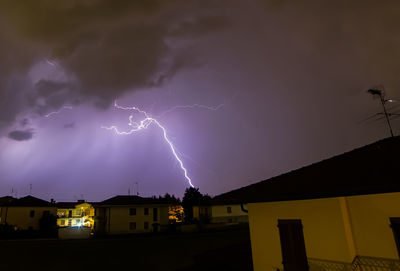 Lightning over illuminated buildings against sky at night