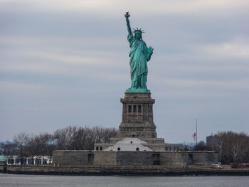 Statue of liberty by lake against sky