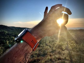 Close-up of hand holding sun against sky during sunset