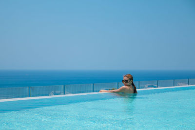 Beautiful woman in infinity pool by sea against clear blue sky