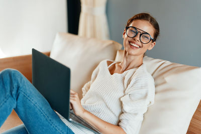 Young woman using laptop while sitting on sofa at home