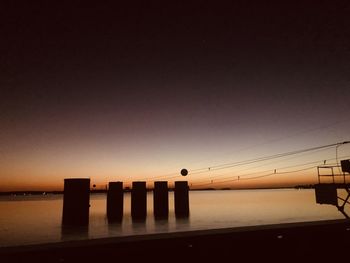 Silhouette wooden posts in sea against clear sky during sunset