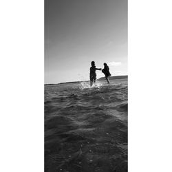 Silhouette men standing on sea against sky