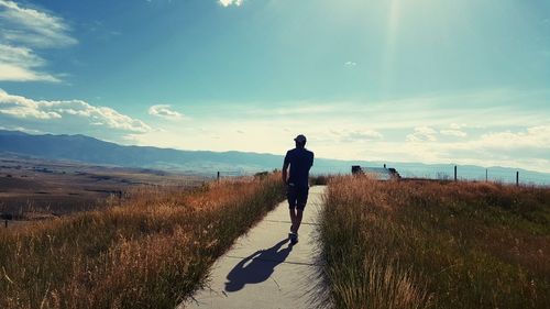 Rear view of man walking on footpath against sky