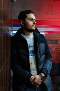 Young man looking away while standing by wall