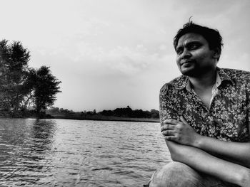 Young man sitting by tree against sky