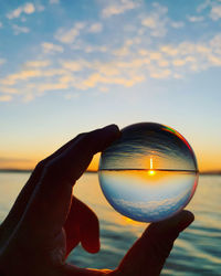 Close-up of man holding crystal ball against sky during sunset