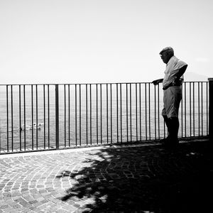 Rear view of man standing by railing against clear sky