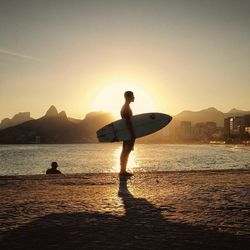 Silhouette people standing on sea shore against clear sky