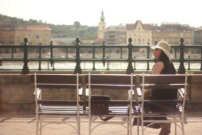 Woman sitting on bench at promenade by river in city