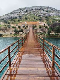 Footbridge leading towards mountain against sky