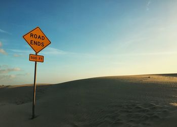 Close-up of road sign on sand at beach against sky