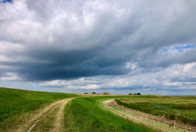 Empty road amidst field against sky