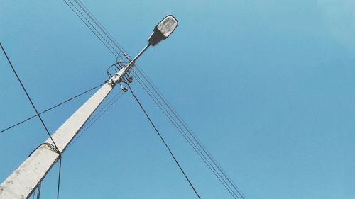 Low angle view of electricity pylon against clear blue sky