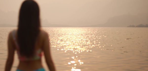 Woman by sea against sky during sunset