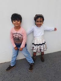 Full length portrait of boy with sister standing against wall