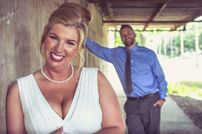 Portrait of bride smiling while groom leaning on wall