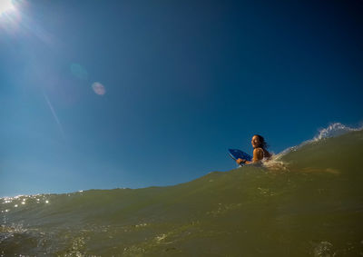 Low angle view of young woman using smart phone against clear blue sky