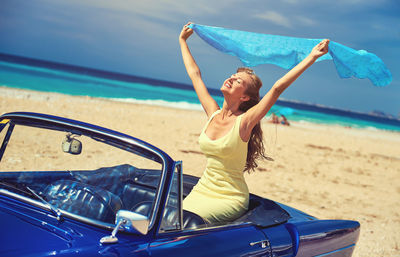 Portrait of smiling young woman in car on beach 