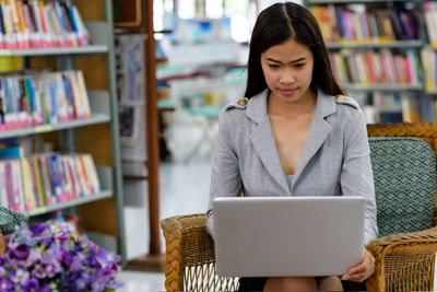 Young woman using phone while sitting on book