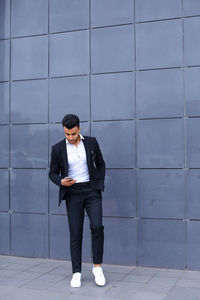 Full length of businessman using mobile phone standing against wall