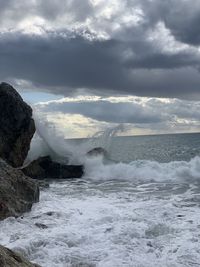 Sea waves splashing on rocks against sky