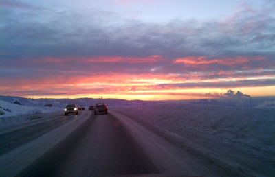 Cars on road against sky during sunset