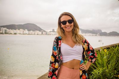 Smiling young woman wearing sunglasses while standing against sky