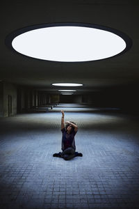 Woman sitting in a building under the light of a skylight.