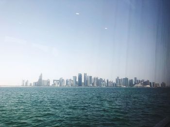 Sea by buildings in city against sky