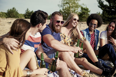 Happy friends with beer bottles sitting at beach