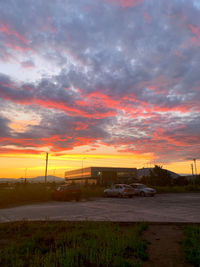 Road by field against dramatic sky during sunset