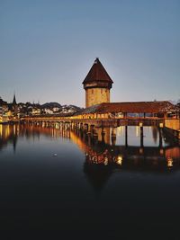 Illuminated building by river against clear sky