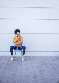 Thoughtful woman with hand on chin sitting in front of wall