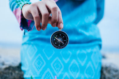 Midsection of woman holding navigational compass at beach against sky