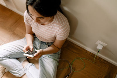 High angle view of girl using smart phone while sitting by wall at home