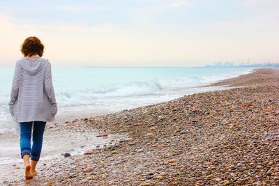 Rear view of woman walking on pebbles at beach during sunset