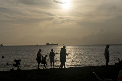 Silhouette people on beach against sky during sunset