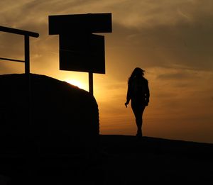 Rear view of silhouette woman standing against orange sky