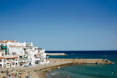 Scenic view of sea by buildings against clear blue sky