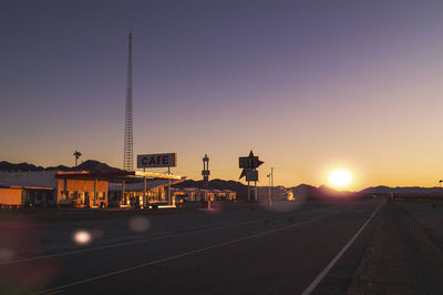 Road by buildings against clear sky during sunset