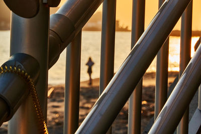 Close-up of metal railing by sea against sky with silhouette people