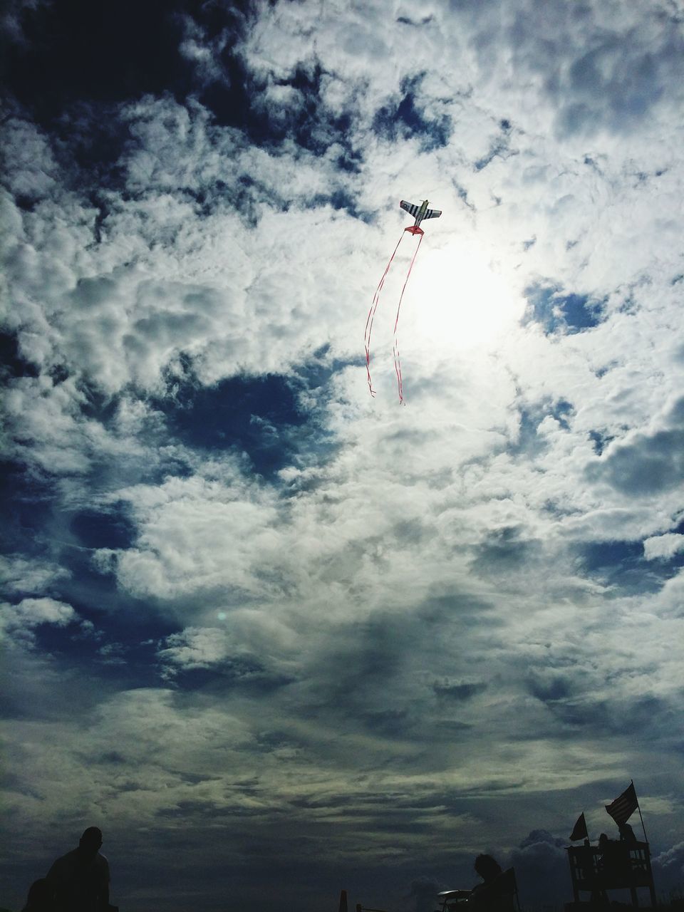 sky, low angle view, cloud - sky, leisure activity, cloudy, flag, lifestyles, men, unrecognizable person, cloud, extreme sports, flying, mid-air, adventure, outdoors, patriotism, parachute, day, travel