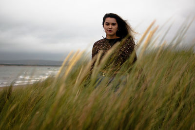 Young woman standing on land against sky with reeds infront 