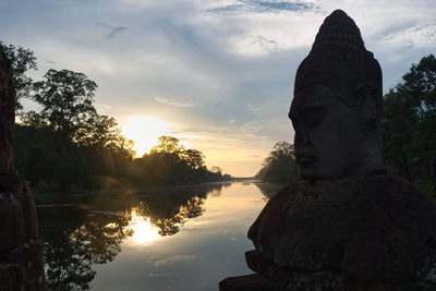 Low angle view of asian statue against sky during sunset with water