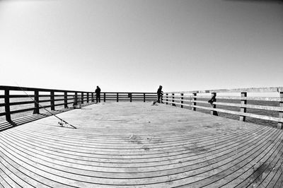 People walking on pier against clear sky