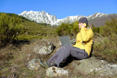 Man talks on the phone and works with a laptop computer in the nature near the snowy mountains