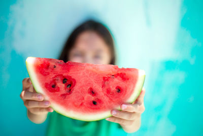 Close-up of girl holding watermelon slice against blue wall