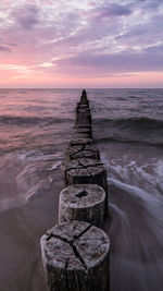 Wooden groyne in sea against sky during sunset